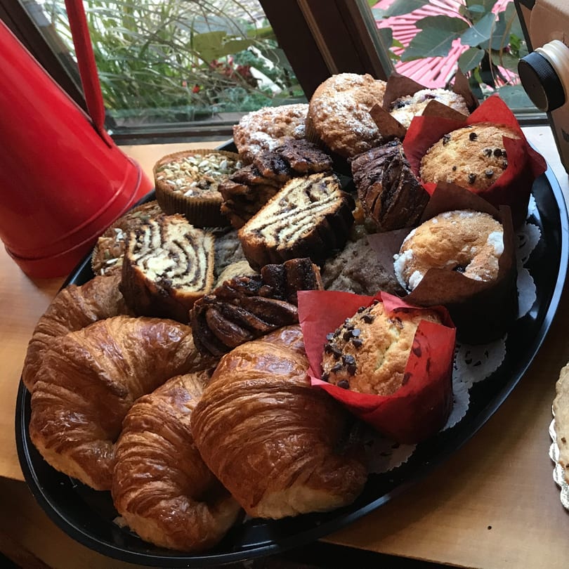 A black tray filled with assorted pastries, including croissants, muffins, and babka slices, by a window.