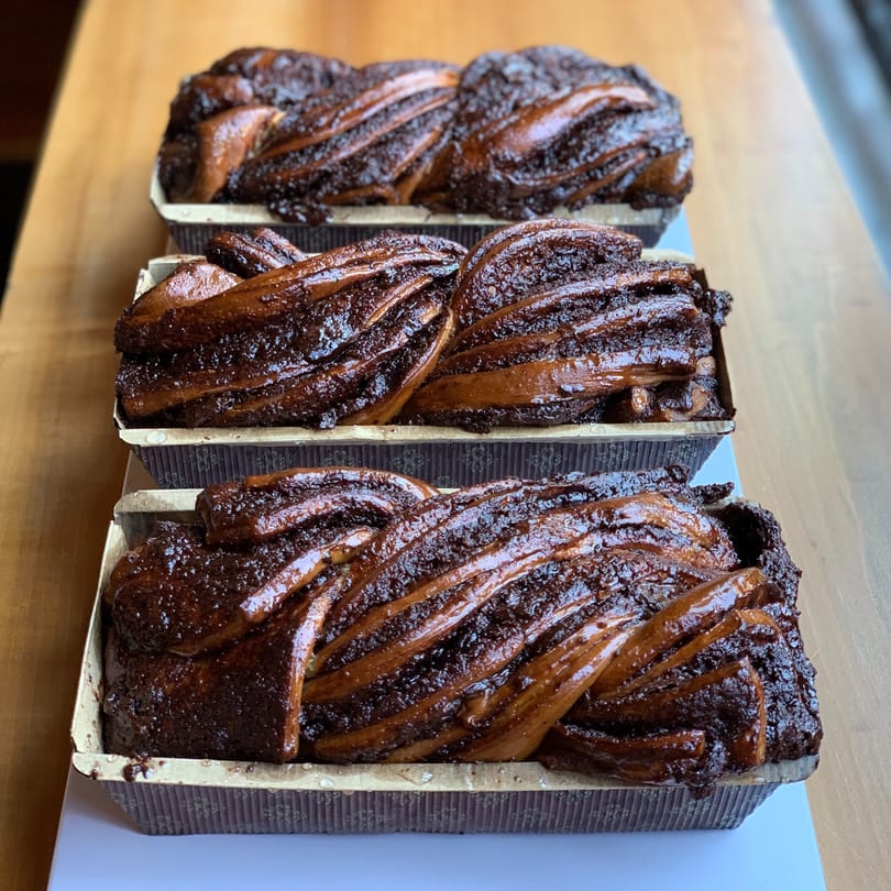 Three freshly baked chocolate babka loaves in paper baking molds on a wooden surface.